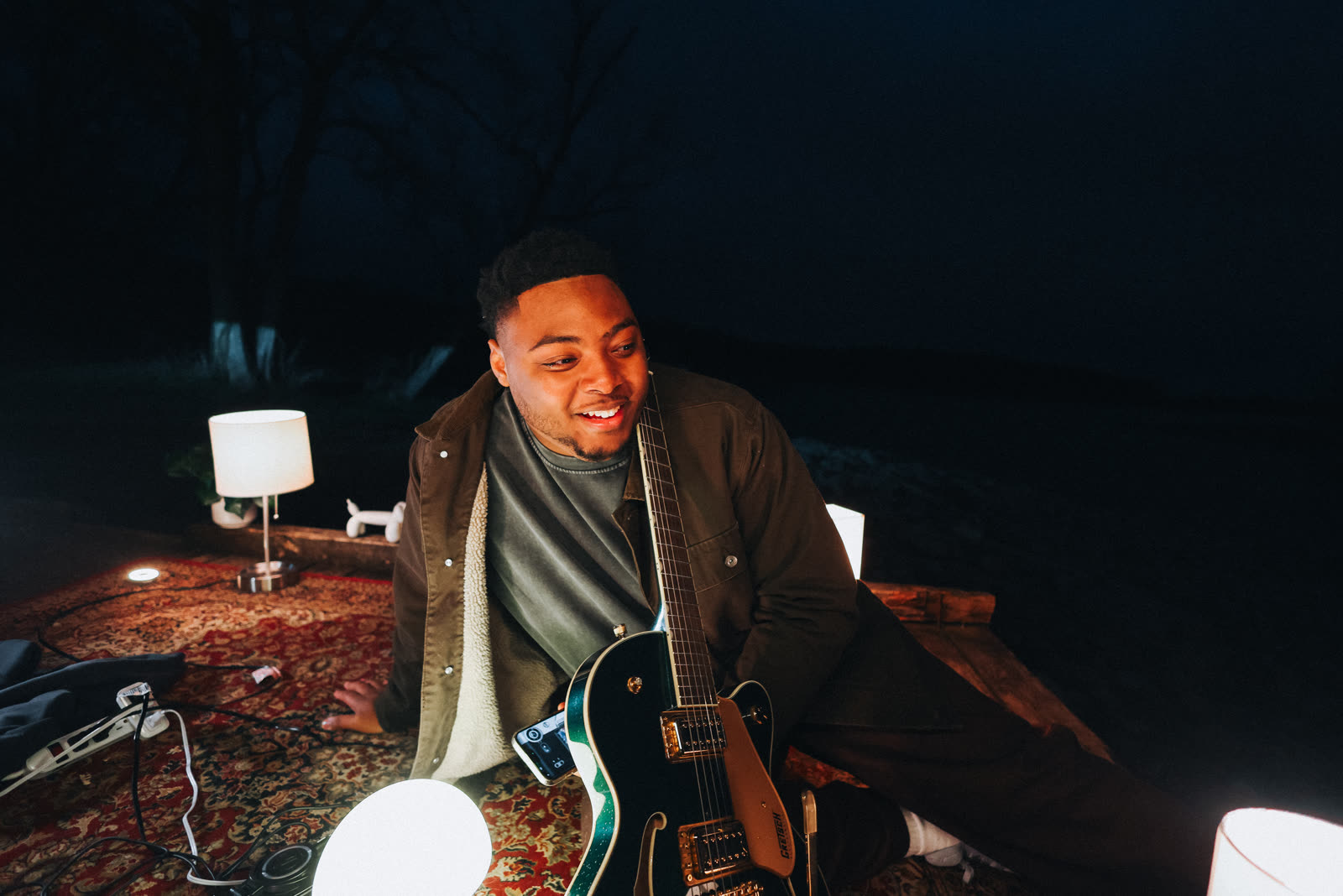 Sincer smiling with his guitar by the lake at night