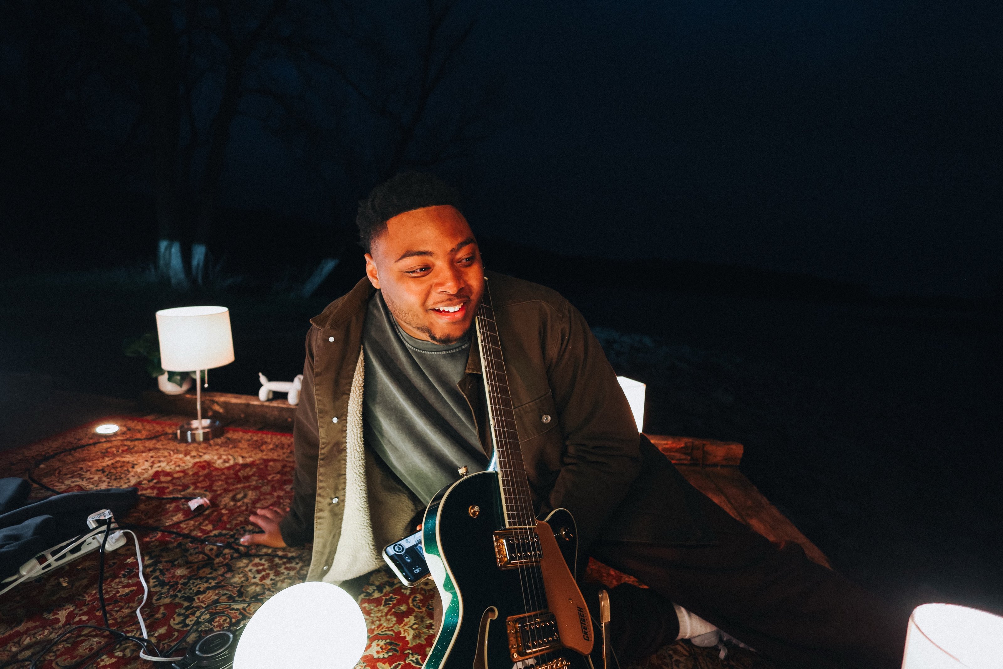 Sincer smiling with his guitar by the lake at night